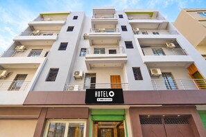 A multi-story hotel building with balconies, air conditioning units, and a sign indicating it is serviced by OVOS. - Deluxe Room The Suncity Hotel (Patna)