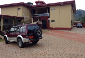 Un SUV color borgoña estacionado frente a un edificio con fachada roja y color crema, una antena parabólica y una entrada con reja.