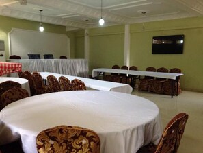 Un salón de conferencias con mesas redondas y sillas, techo blanco y una televisión de pantalla plana en la pared.