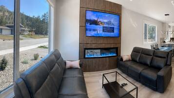 A modern living room with a large TV, two sofas, and a glass coffee table.