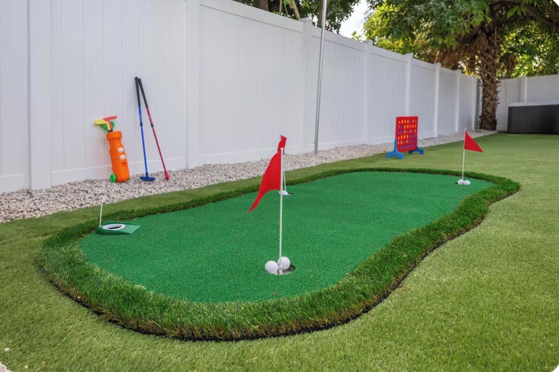 A miniature golf course with a green artificial turf, red flags, and a white fence in the background.
