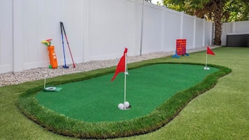 A miniature golf course with a green artificial turf, red flags, and a white fence in the background.