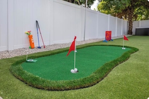 Un parcours de mini-golf avec un gazon synthétique vert, des drapeaux rouges et une clôture blanche en arrière-plan.