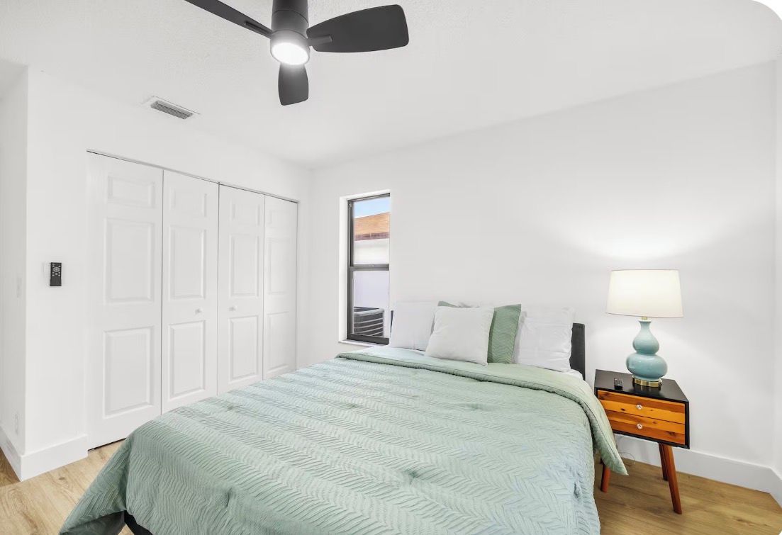 A bedroom with a bed, a nightstand, a ceiling fan, and a window.