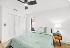 Ein Schlafzimmer mit einem Bett, einem Nachttisch, einem Deckenventilator und einem Fenster.