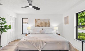 Une chambre à coucher avec un lit, un ventilateur de plafond, une fenêtre donnant sur un beau paysage et une œuvre d’art accrochée au mur.