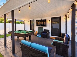 Eine Terrassengruppe im Freien mit Billardtisch, Korbmöbeln und Lichterketten.