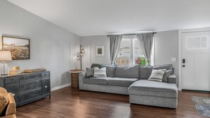 Ein Wohnzimmer mit einem grauen Sofa, einer dunklen Holzkommode und einer Lampe.