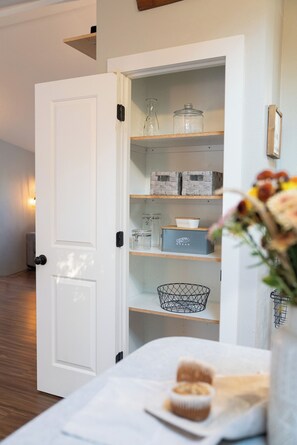 A white interior space with a door leading to a storage area containing shelves, jars, and a bread box. - Hidden Haven | Made for Families + Outdoor Retreat (Molalla)
