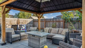 An outdoor patio with wicker furniture, a glass-top table, and a wooden pergola. - Hidden Haven | Made for Families + Outdoor Retreat (Molalla)