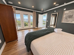 A bedroom with a bed, a wardrobe, and a large window with a view.