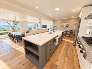 A modern kitchen with a large island, wooden flooring, and a view of the outdoors.
