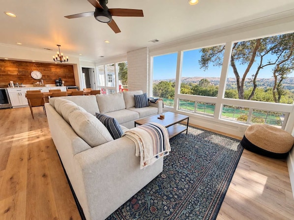 A spacious living area with a large sofa, a coffee table, and a view of a landscape through large windows.