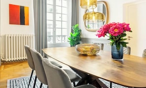 Een eethoek met een houten tafel, stoelen, een vaas met bloemen, een decoratieve schaal en een radiator.