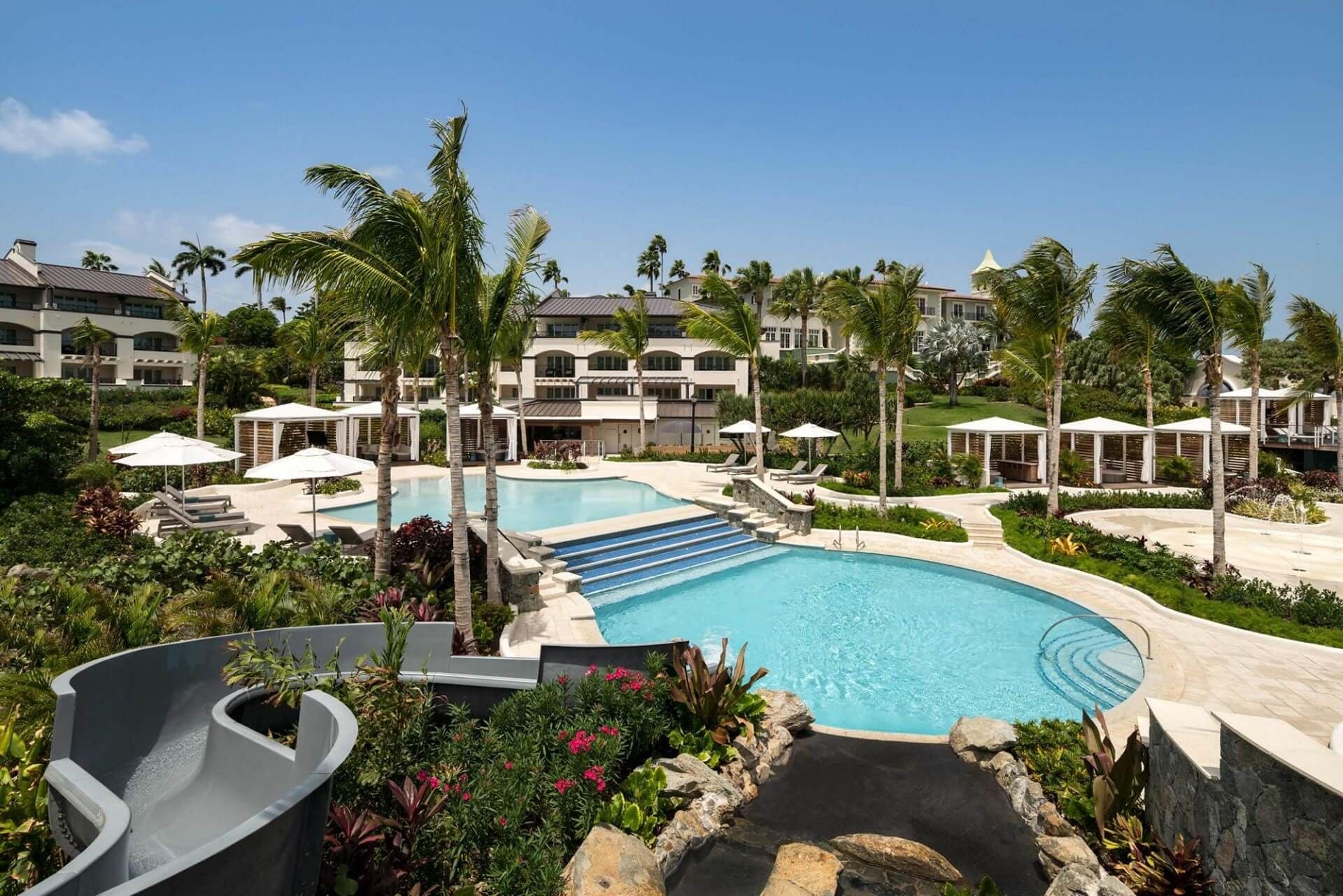 A resort with a large pool, palm trees, and multiple buildings with balconies.