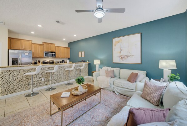 A modern living room with a sofa, coffee table, and a kitchen area with bar stools. - Spacious 4BR Retreat | Pool | Disney & Universal (Kissimmee)