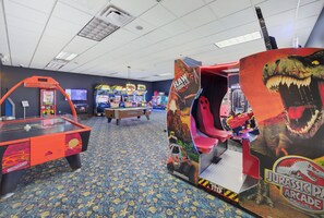 A gaming arcade with various machines, including a 'Jurassic Park' themed ride. - Spacious 4BR Retreat | Pool | Disney & Universal (Kissimmee)