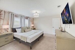 A bedroom with a bed, bedside tables, a chandelier, a television, and a door. - Spacious 4BR Retreat | Pool | Disney & Universal (Kissimmee)