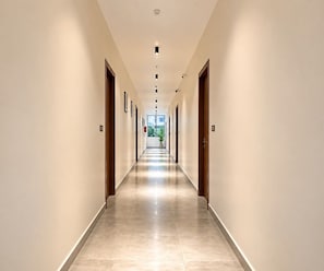 A long, narrow hotel corridor with doors on both sides, a tiled floor, and recessed lighting on the ceiling. - Super Deluxe Room V Stays (Chittoor)