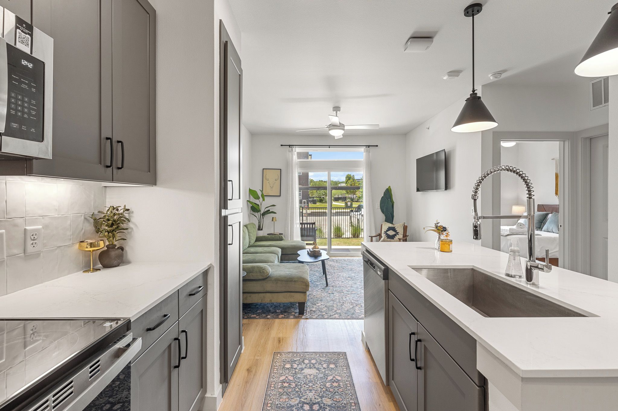 A modern kitchen with a central island, a dining area with a view, and a living space with a sofa and a TV.