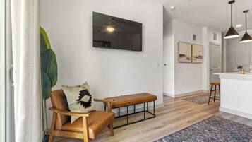 A modern living room with a wooden bench, a television mounted on the wall, and a large plant.