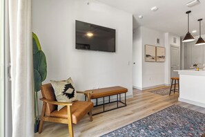 A modern living room with a wooden bench, a television mounted on the wall, and a large plant. - Luxury 1 Bed with Walkout Garden MER 9115 (San Marcos)