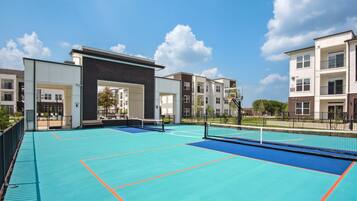 A tennis court with a net, surrounded by apartment buildings.