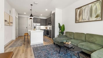Een moderne woonkamer met een groene bank, een salontafel en een keuken op de achtergrond.