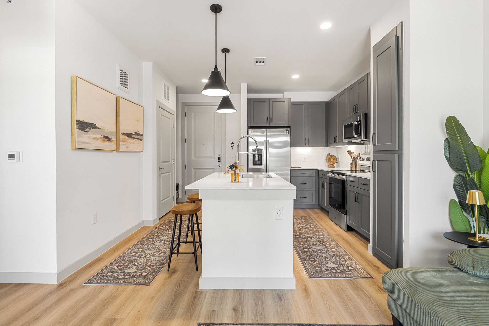 A modern kitchen with a central island, grey cabinetry, stainless steel appliances, and a bar stool.