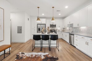 A modern kitchen with white cabinetry, stainless steel appliances, and a central island with bar stools. - Modern 2BR 2BA | Open Layout  MER 1307 (San Marcos)