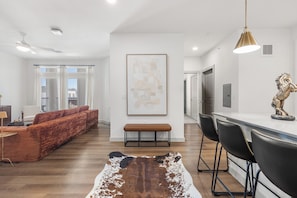 A modern living room with a sofa, a bench, and a dining area with chairs and a table. - Modern 2BR 2BA | Open Layout MER 1307 (San Marcos)