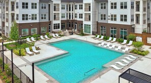 A multi-story residential building with a swimming pool surrounded by lounge chairs. - Modern 2BR 2BA | Open Layout  MER 1307 (San Marcos)