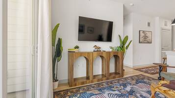A living room with a flat-screen TV mounted on the wall, a wooden console table with three arches, and a patterned rug on the floor.