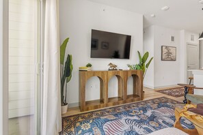 Een woonkamer met een flatscreen televisie aan de muur, een houten console met drie bogen, en een vloerkleed met een patroon.