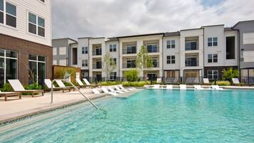 A swimming pool with lounge chairs and a building with multiple balconies.