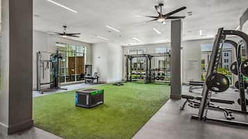 Un gimnasio con equipos de ejercicio variados, una zona de césped artificial verde y amplias ventanas.
