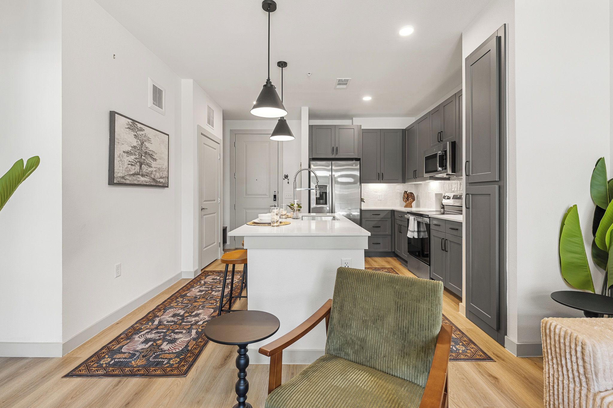 A modern kitchen with a central island, grey cabinets, stainless steel appliances, and a dining area with a chair and table.