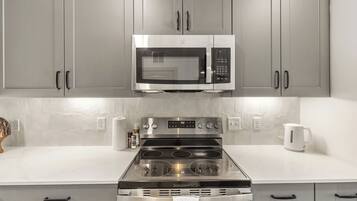 A kitchen with grey cabinets, a stainless steel microwave, a gas stove, and a white countertop.