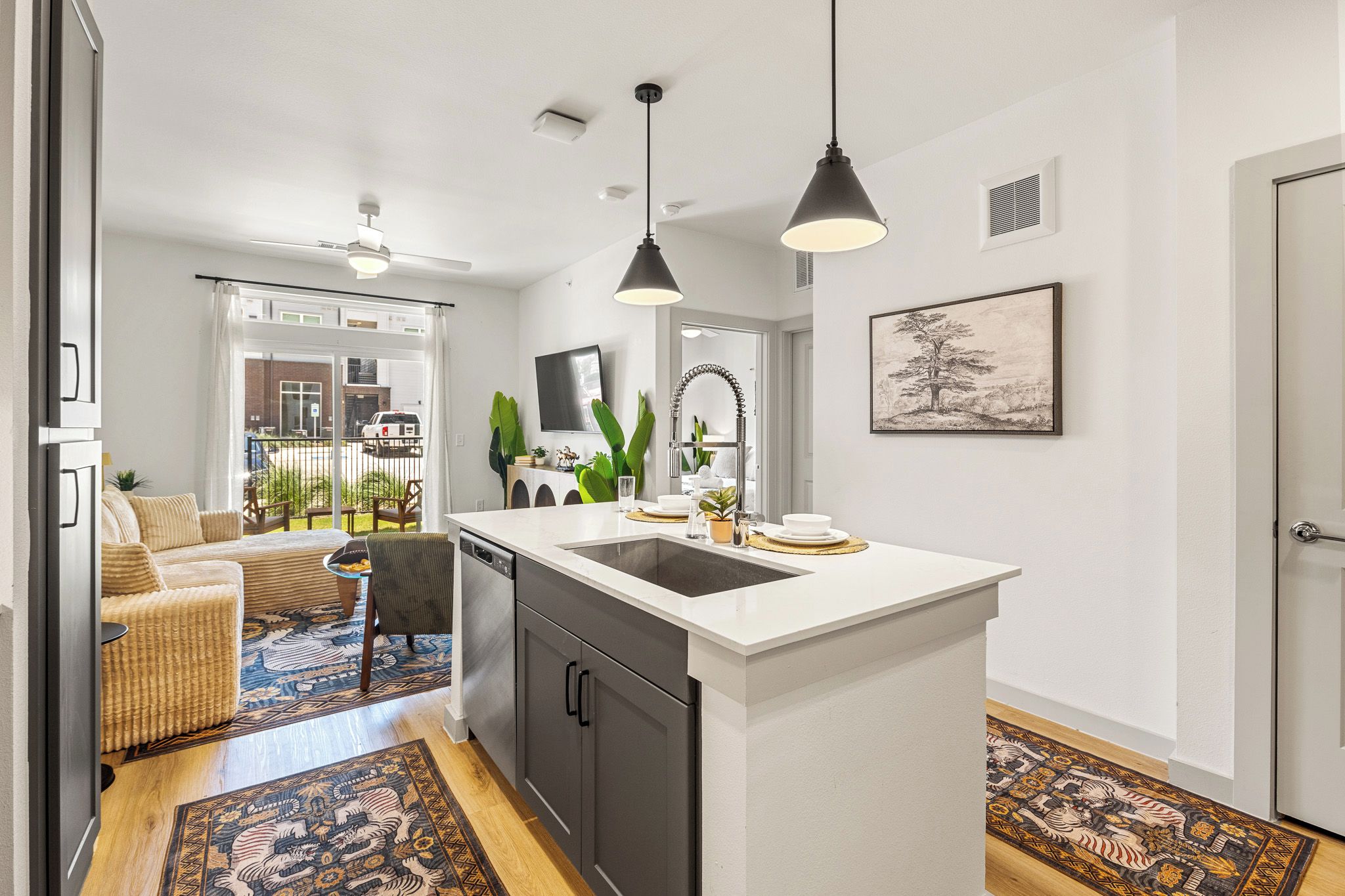 A modern kitchen with a central island, a dining area with a sofa and chairs, and a living room with a TV and plants.