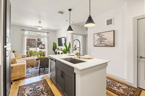 Een moderne keuken met een centraal eiland, een zithoek met een bank en stoelen, en een woonkamer met een televisie en planten.