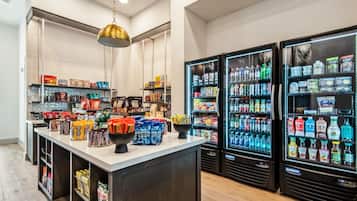 A well-stocked beverage refrigerator with various drinks, a central counter with snacks and packaged goods, and a hanging light fixture.