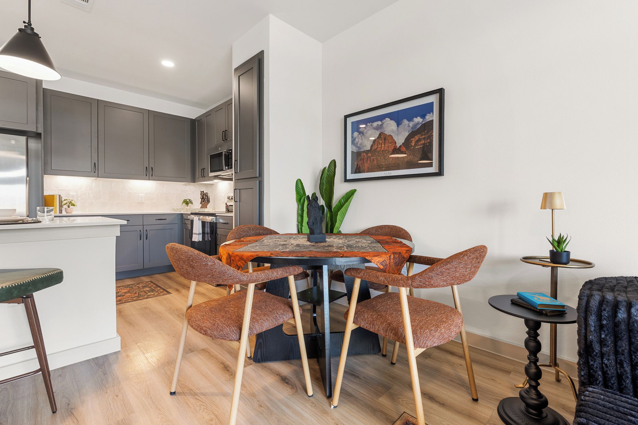 A modern kitchen with grey cabinets, a white countertop, and a dining area with a round table and wicker chairs.