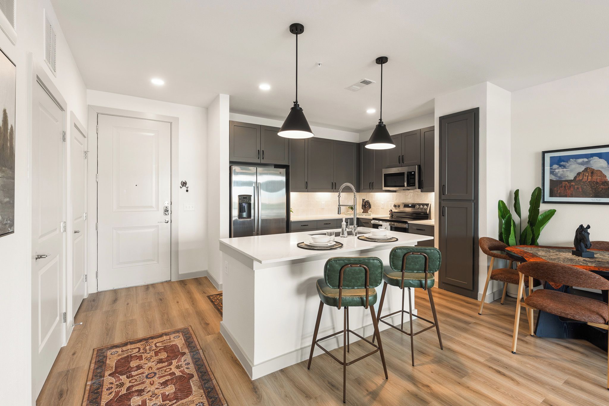 A modern kitchen with a central island, bar stools, and a dining table with chairs.