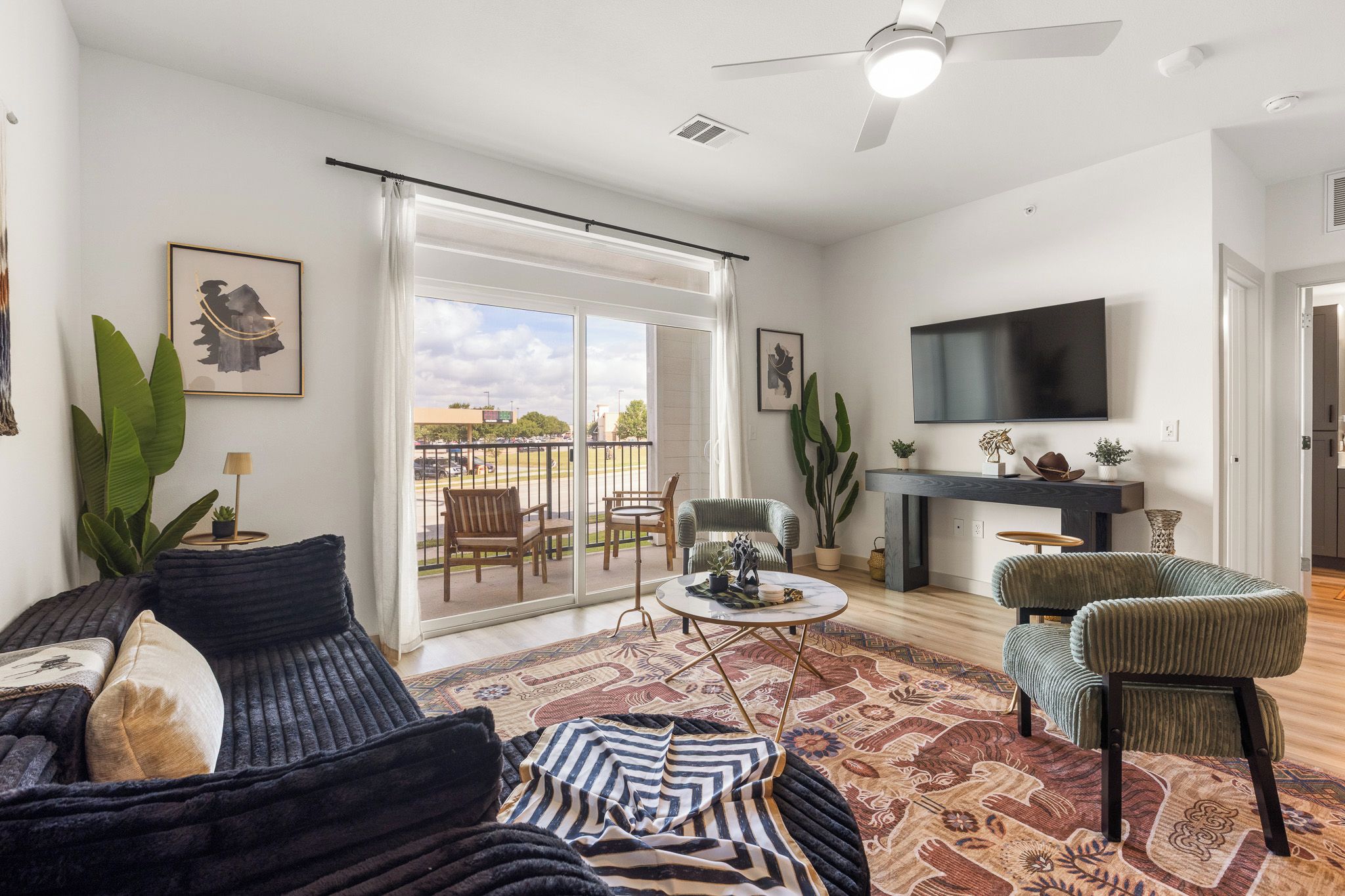 A spacious living room with a large sliding glass door to the outside, a flat-screen TV mounted on the wall, and a comfortable seating area with a sofa and chairs.