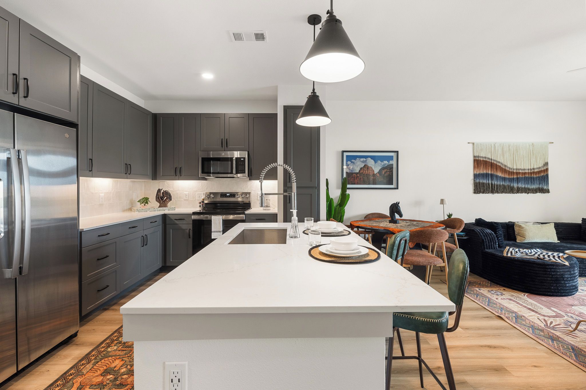 Een moderne keuken met een centraal eiland, roestvrijstalen apparatuur en een zithoek met een bank en stoelen.