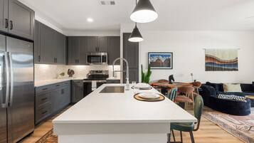 Een moderne keuken met een centraal eiland, roestvrijstalen apparatuur en een zithoek met een bank en stoelen.