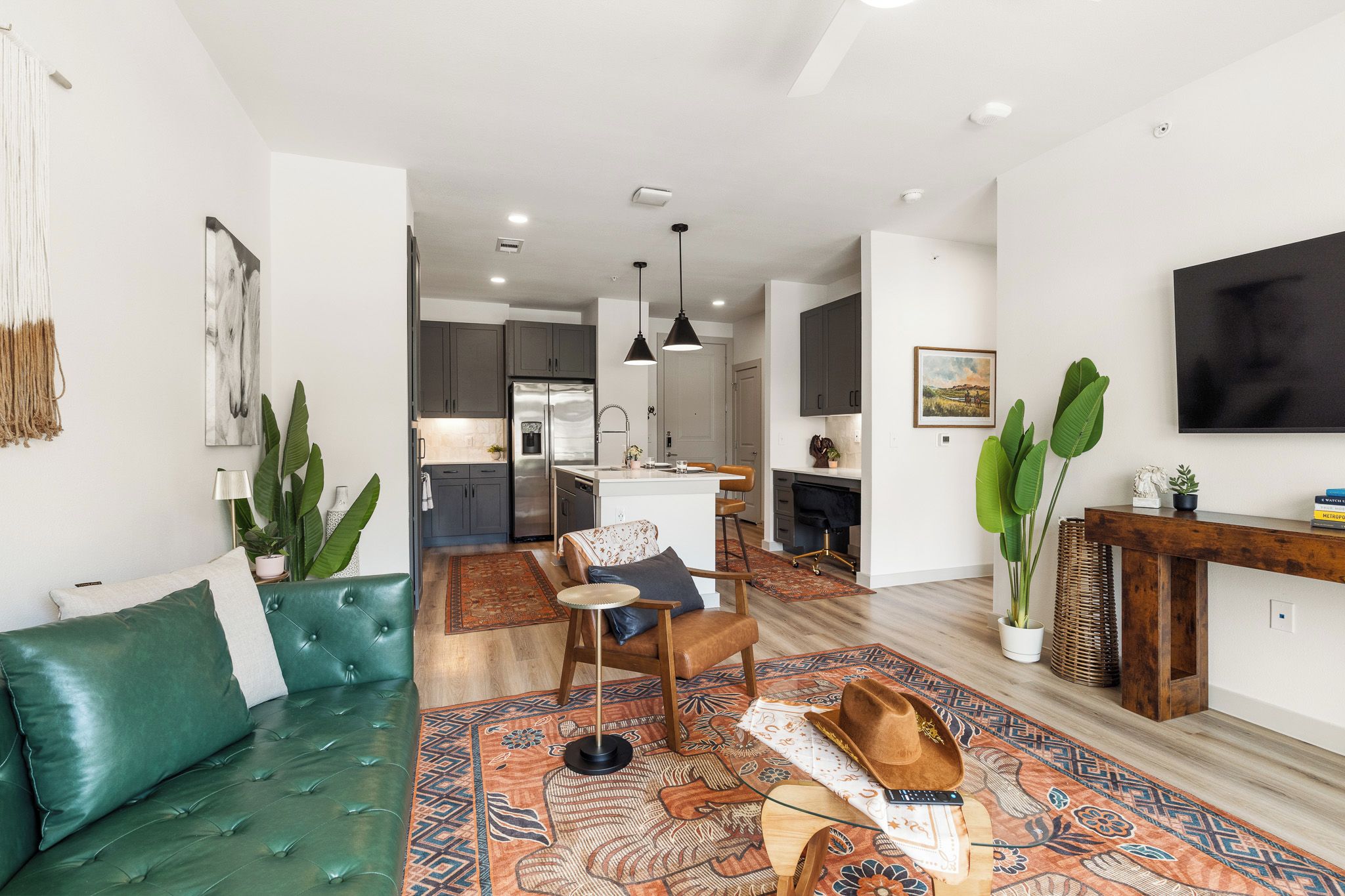 A modern living room with a green sofa, a patterned rug, and a dining area with a wooden table and chairs.