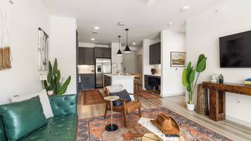 A modern living room with a green sofa, a patterned rug, and a dining area with a wooden table and chairs.