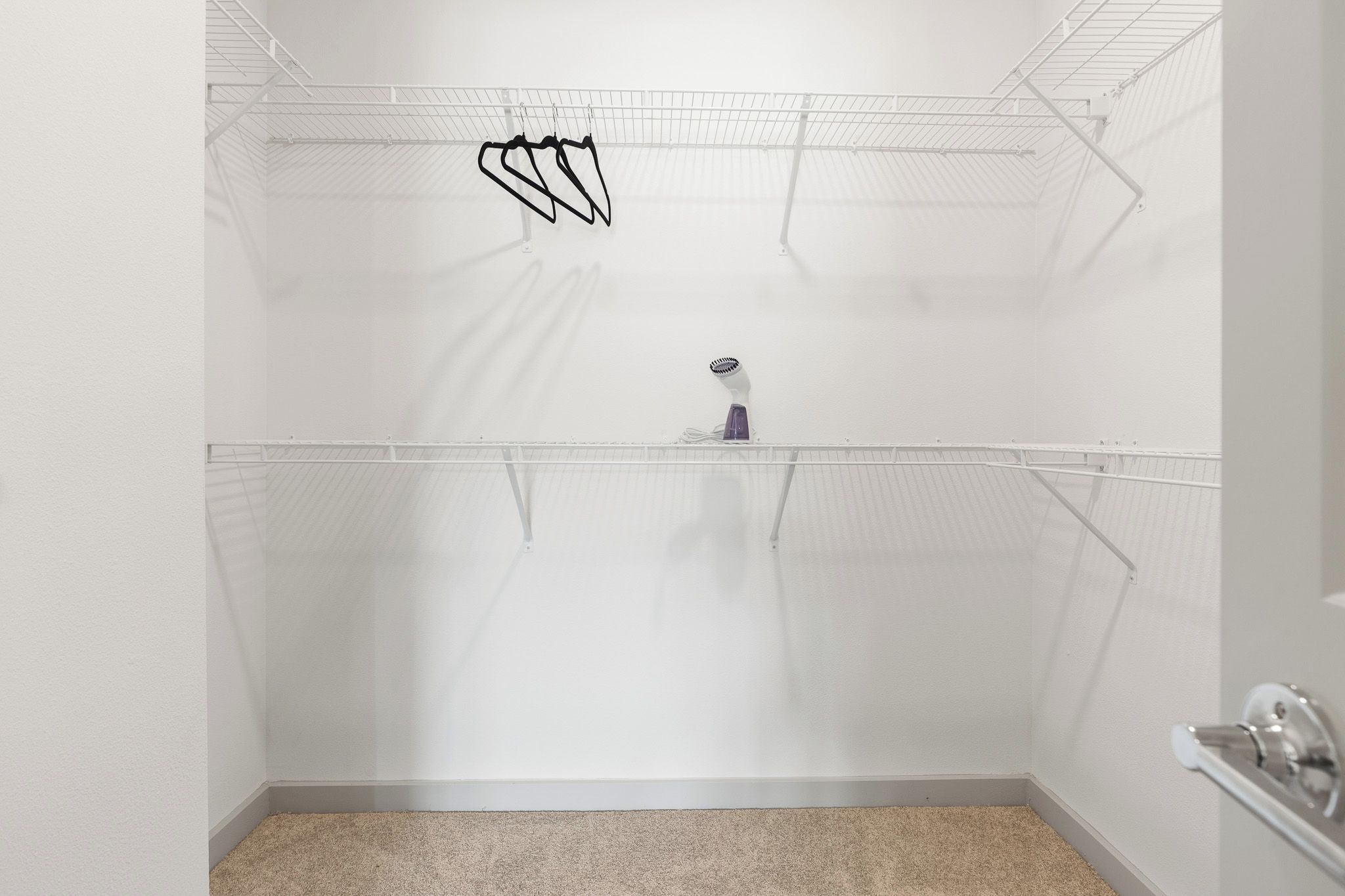 A corner closet with wire shelving, a vacuum cleaner, and a beige carpet.