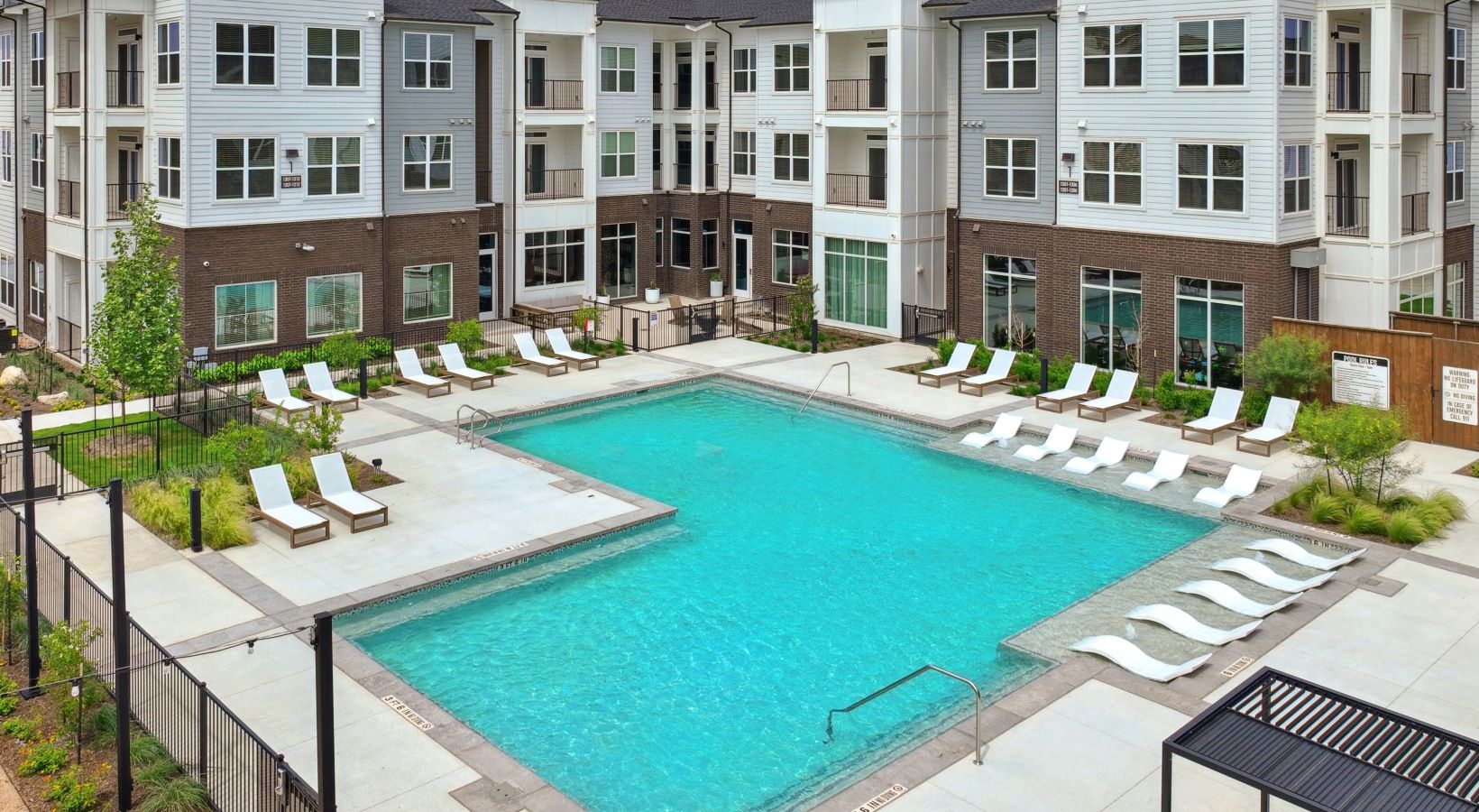 Un edificio residencial de varios pisos con piscina rodeada de sillones de descanso.